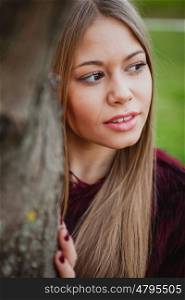 Portrait blonde girl next to a tree trunk in a park