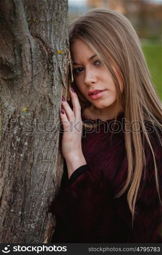 Portrait blonde girl next to a tree trunk in a park