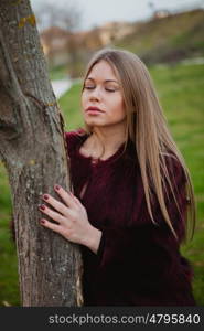 Portrait blonde girl next to a tree trunk in a park