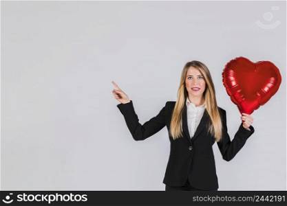 portrait blonde young businesswoman holding red foil balloon hand pointing her finger