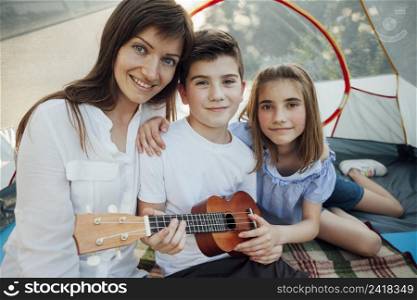 portrait brother sister holding ukulele sitting with their mother tent