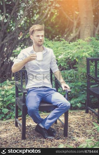 Portrait business young handsome man drink cup of coffee sitting in the park, relax and leisure concept.