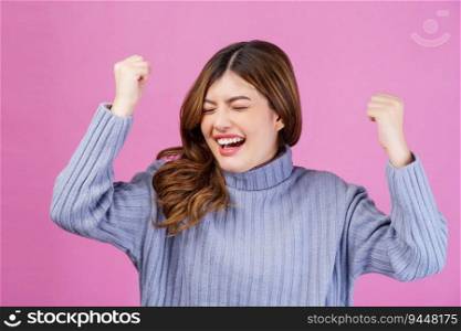 Portrait close-up of cheerful positive young woman standing and making winner gesture isolated over pink background. Life people energy and success concept.