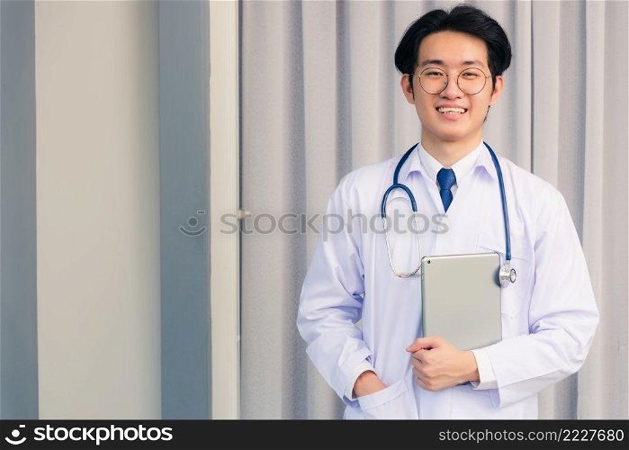 Portrait closeup of Happy Asian young doctor handsome man smiling in uniform and stethoscope neck strap holding smart digital tablet on hand and looking to the camera, healthcare medicine concept