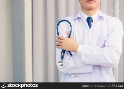 Portrait closeup of Happy Asian young doctor handsome man smiling in uniform stand crossed arm hold stethoscope on hand looking to camera with cop space, healthcare medicine concept