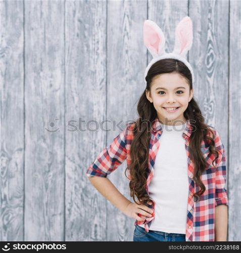 portrait confident smiling girl with bunny ear head against wooden backdrop