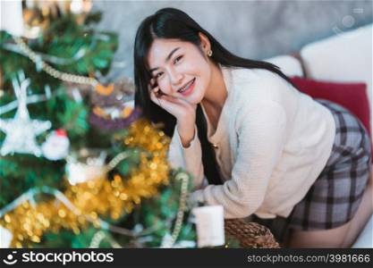 Portrait Cute beautiful positive smile young asian woman decorating to a Christmas tree at home in the living room indoors Decoration During Christmas x-mas and New Year holidays.