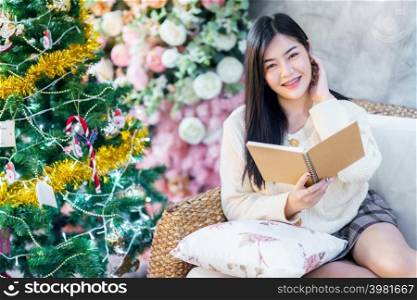 Portrait Cute beautiful positive smile young asian woman holding of read a book at home in the living room indoors Decoration During Christmas x-mas and New Year holidays.