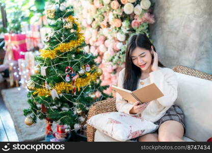 Portrait Cute beautiful positive smile young asian woman holding of read a book at home in the living room indoors Decoration During Christmas x-mas and New Year holidays.