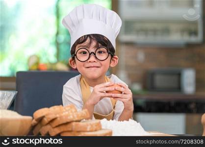 Portrait cute little Asian happy boy interested in cooking funny in home kitchen. People lifestyles and Family. Homemade food and ingredients concept. Baking Christmas cake and cookies. Smiling child