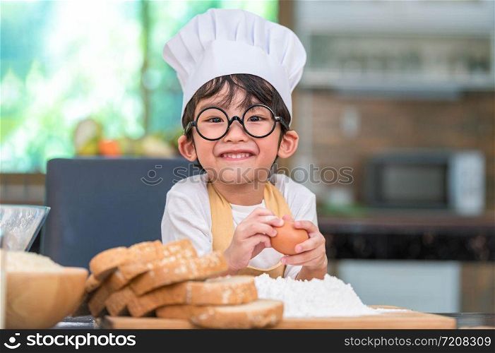 Portrait cute little Asian happy boy interested in cooking funny in home kitchen. People lifestyles and Family. Homemade food and ingredients concept. Baking Christmas cake and cookies. Smiling child