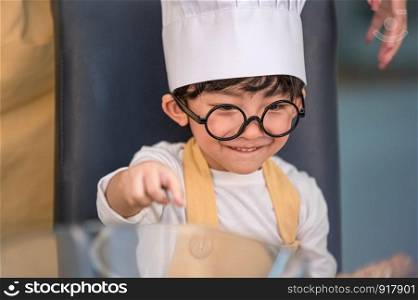 Portrait cute little Asian happy boy interested in cooking with mother funny in home kitchen. People lifestyles and Family. Homemade food and ingredients concept. Baking Christmas cake and cookies