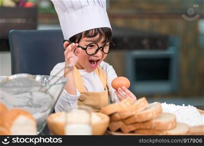 Portrait cute little Asian happy boy surprised and interested in cooking funny in home kitchen. People lifestyles and Family. Homemade food and ingredients concept. Baking Christmas cake and cookies