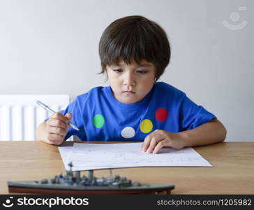 Portrait Cute little schoolboy drawing battleship, Child playing with model ship toy and sketching on paper, Indoors actvitiy concept