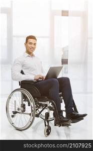 portrait disabled smiling young businessman sitting wheelchair using laptop office
