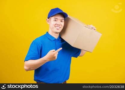 Portrait excited delivery happy man logistic standing he smile wearing blue t-shirt and cap uniform holding parcel box pointing finger to the box, studio shot isolated on yellow background