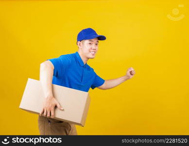 Portrait excited delivery happy man logistic standing smile wearing blue t-shirt and cap uniform holding parcel box and running looking to camera, studio shot isolated on yellow background, side view