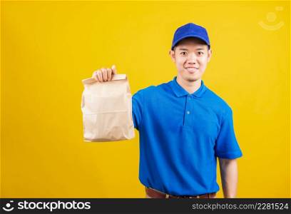 Portrait excited delivery service man smile wearing blue t-shirt and cap uniform hold paper containers for takeaway bag grocery food packet looking to camera, studio shot isolated on yellow background