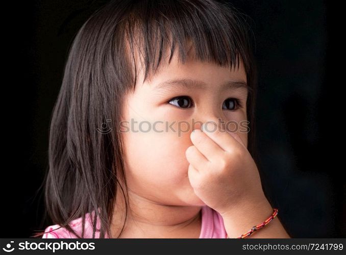 Portrait face of Asian little child girl holding her nose because of a bad smell on dark background.