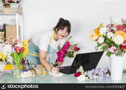 portrait female florist with flowers writing notepad
