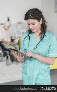 portrait female nurse with stethoscope around her neck using digital tablet