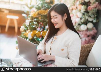 Portrait freelance business smile young asian woman holding cup coffee online working with laptop computer at home in the living room indoors Decoration During Christmas x-mas and New Year holidays.