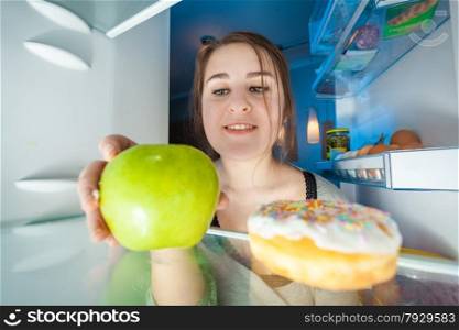 Portrait from inside the fridge of woman taking green apple