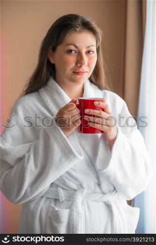 portrait girl in bathrobe with a cup near the window