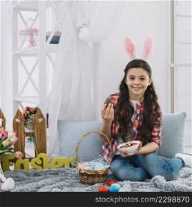 portrait girl sitting bed holding easter chocolate egg bowl candies looking camera