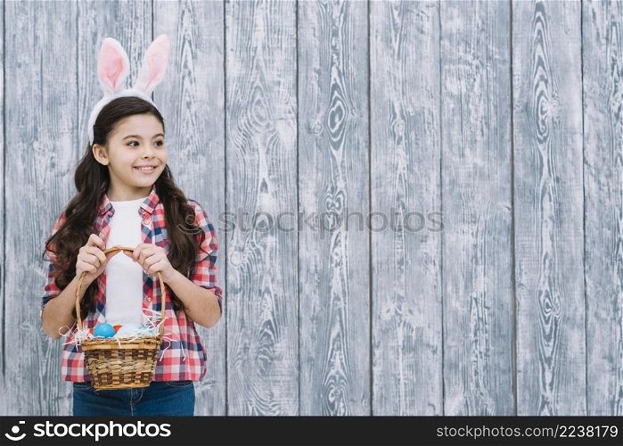 portrait girl with bunny ears holding easter eggs basket looking away