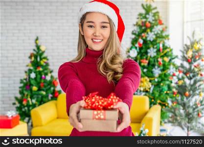 Portrait happiness asian woman wearing colorful red sweaters with hat holding and giving the gift box to other for merry christmas celebration, asian or asean indoors party, xmas and new year concept