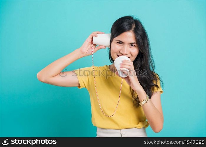Portrait happy Asian beautiful young woman smile white teeth standing wear yellow t-shirt, She holding paper can telephone for talking, studio shot on blue background with copy space for text