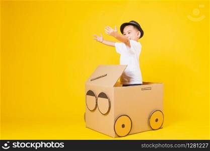 Portrait happy Asian cute little children boy smile so happy wearing white T-shirt driving car creative by cardboard, studio shot on yellow background with copy space