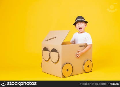 Portrait happy Asian cute little children boy smile so happy wearing white T-shirt driving car creative by cardboard, studio shot on yellow background with copy space