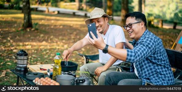 Portrait happy Asian man friends Making a video call with smartphone in c&ing. Cooking set front ground. Outdoor cooking, traveling, c&ing, lifestyle concept.