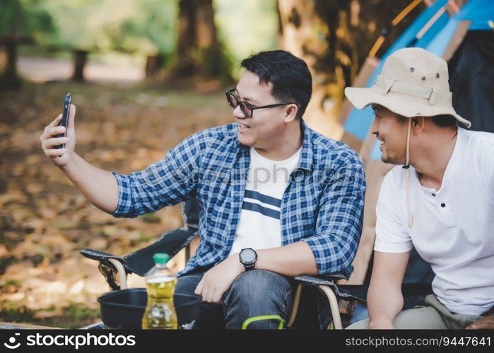 Portrait happy Asian man friends Making a video call with smartphone in c&ing. Cooking set front ground. Outdoor cooking, traveling, c&ing, lifestyle concept.