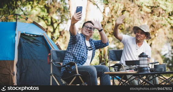 Portrait happy Asian man friends Making a video call with smartphone in c&ing. Cooking set front ground. Outdoor cooking, traveling, c&ing, lifestyle concept.