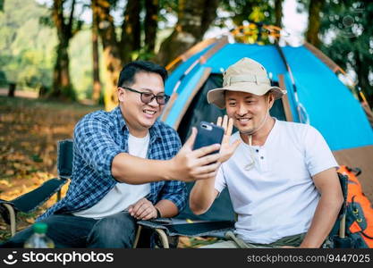 Portrait happy Asian man friends Making a video call with smartphone in camping. Cooking set front ground. Outdoor cooking, traveling, camping, lifestyle concept.