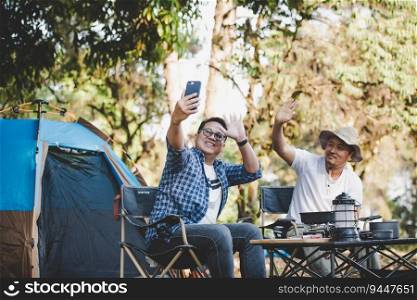 Portrait happy Asian man friends Making a video call with smartphone in camping. Cooking set front ground. Outdoor cooking, traveling, camping, lifestyle concept.