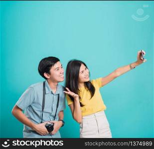Portrait happy Asian young handsome man, beautiful woman couple smile standing wear shirt, taking selfie photo on a smartphone, studio shot on blue background with copy space
