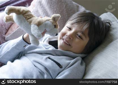 Portrait Happy boy lying on sofa playing with dog toy, Healthy child boy playing with his toy relaxing at home on weekend, Relax, warm and cozy scene at home concept