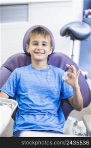 portrait happy boy sitting dental chair gesturing ok sign
