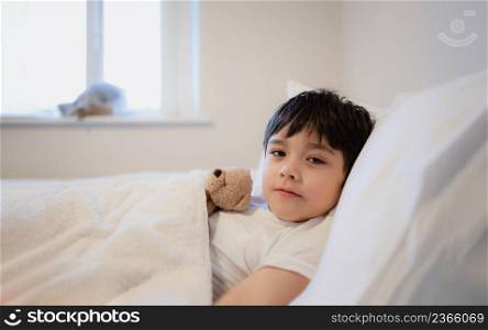 Portrait happy Child boy lying in bed with teddy bear looking at camera with smiling face, Healthy Kid wake up with happy face, Children health care concept