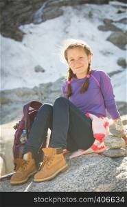 portrait happy girl hiker with a backpack sitting on a rock with snow and mountains in the background, Norway