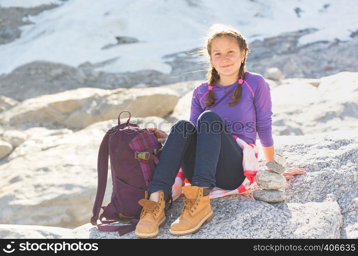 portrait happy girl hiker with a backpack sitting on a rock with snow and mountains in the background, Norway