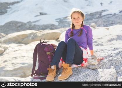 portrait happy girl hiker with a backpack sitting on a rock with snow and mountains in the background, Norway