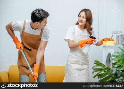 Portrait happy smiling young couple with equipment for cleaning house, they wearing rubber gloves, pretty woman hold spary bottle in hand, They smile with happy together