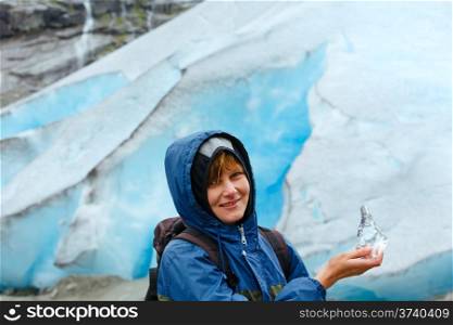 Portrait happy woman with piece of ice in hand on Nigardsbreen glacier background (Norway)