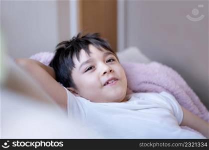 Portrait happy yong boy lying on sofa relaxing at home, Head shot cute kid looking at camera with smiling face, Positive child sitting on couch having fun on weekend