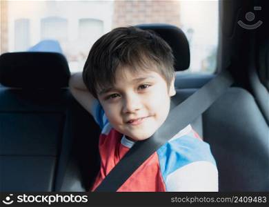 Portrait Happy Young boy siting in safety car seat looking at camera with smiling face,Child sitting in the back passenger seat with a safety belt, School kid traveling to school by car.Back to school